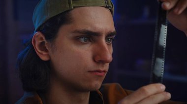 Şapka takan genç bir adam film şeridini yakından inceleyerek fotoğrafçılığa olan merak ve tutkuyu vurguluyor..