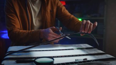 Bir adam, filmi, loş bir fotoğraf stüdyosunda makasla dikkatlice kesiyor..