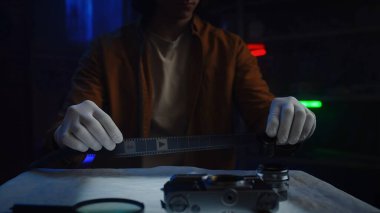 Eldiven giyen bir insan, loş bir fotoğraf stüdyosundaki film şeridini dikkatle tutar..