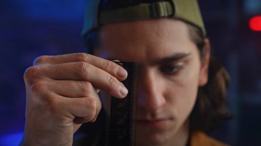 Genç bir adam loş bir odada bir film şeridini dikkatle inceliyor, film yapımında odak ve merak olduğunu gösteriyor. Kapat.