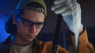 Genç bir adam loş bir odada bir film şeridini dikkatle inceliyor, film yapımında odaklanma ve merak öneriyor..