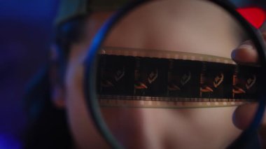 Büyüteçle incelenen eski bir film şeridinin yakından görüntüsü. Film analizinin ve korunmanın özünü yakalar. Yaklaşın, ağır çekim.