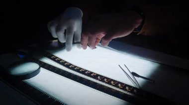 Eldivenli eller ve hassas aletlerle ışık masasında yakından incelenen bir film şeridinin karmaşık görüntüsü. Yavaş çekim