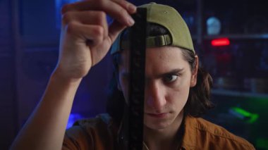 Genç bir adam loş bir odada bir film şeridini dikkatle inceliyor, film yapımında odaklanma ve merak öneriyor..