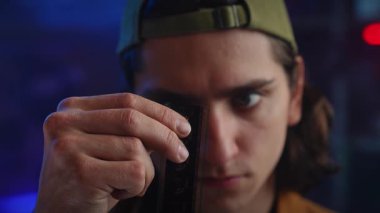 Genç bir adam loş bir odada bir film şeridini dikkatle inceliyor, film yapımında odak ve merak olduğunu gösteriyor. Kapat.