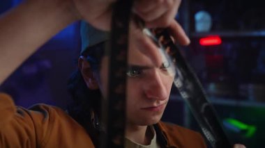 Genç bir adam loş bir odada bir film şeridini dikkatle inceliyor, film yapımında odaklanma ve merak öneriyor..