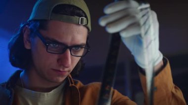 Genç bir adam loş bir odada bir film şeridini dikkatle inceliyor, film yapımında odaklanma ve merak öneriyor..