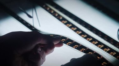 Bir insan büyüteçle bir film şeridini yakından inceler ve her karenin detaylarını ortaya çıkarır..