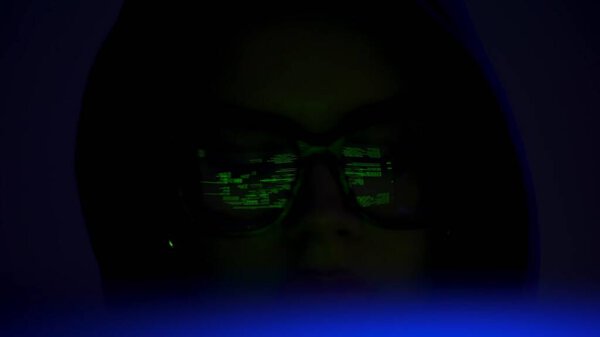 Крупный план изображения загадочного кодировщика в темной среде, с зеленым кодом, отражающимся от очков, вызывающим темы кибербезопасности и взлома.