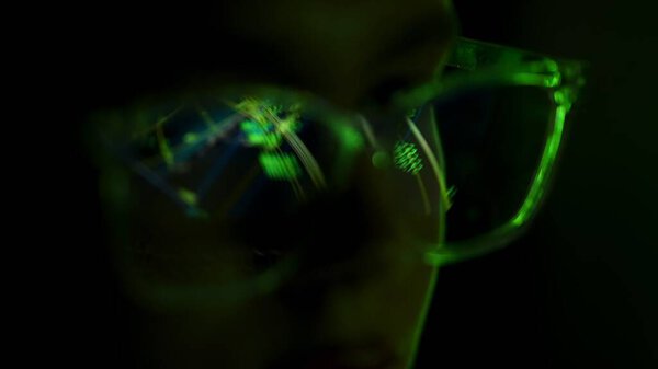 Закрытие очков, отражающих ярко-зеленые цифровые узоры, символизирующие анализ данных и технологии в тусклом освещении.