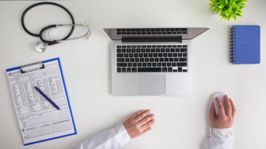 Bir dizüstü bilgisayar, steteskop, tıbbi formlar ve profesyonel bir sağlık ortamını gösteren bir defter içeren temiz bir masa düzeni. Üst çekim