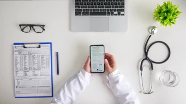Bir sağlık uzmanı hasta bilgilerine ulaşmak için akıllı telefon kullanıyor ve modern tıbbi uygulamaları gösteriyor. Üst çekim