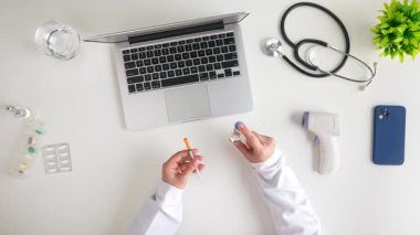 Sağlık çalışanlarını temsil eden şırınga, tüp, steteskop ve dizüstü bilgisayar gibi tıbbi aletlerle dolu bir masa. Üst çekim