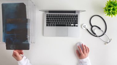 Bir doktor, dizkapağı, stetoskop ve bitkiyle dolu, düzenli bir muayenehanede diz ekleminin röntgenini inceler. Üst çekim