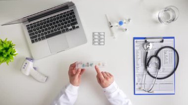 Bir dizüstü bilgisayar, steteskoplu bir pano ve ilaç organizatörünün yer aldığı tıbbi profesyonellerin genel görünümü. Üst çekim