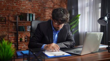 Kendini işine adamış bir birey, modern ofis ortamında bir masaya notlar yazarken görülüyor. Konsantrasyon ve verimliliği vurguluyor..