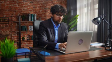 Odaklanmış bir işadamı masasında strateji tasarlar. Ofis modern, dizüstü bilgisayarı ve düzgün düzenlenmiş belgeleri var..