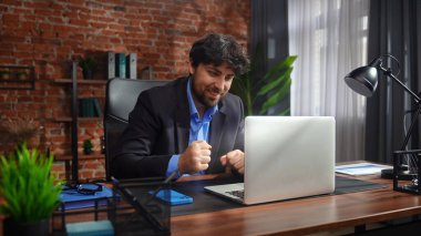 Odaklanmış bir işadamı masasında strateji tasarlar. Ofis modern, dizüstü bilgisayarı ve düzgün düzenlenmiş belgeleri var..