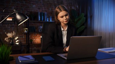 Masasında odaklanmış iş kadını düşünme stratejisi, yorgun görünüyor. Dizüstü bilgisayarı ve düzgün düzenlenmiş belgeleri olan modern ofis.