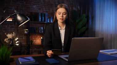 Odaklanmış bir iş kadını masasında strateji düşünüyor. Ofis modern, dizüstü bilgisayarı ve düzgün düzenlenmiş belgeleri var..