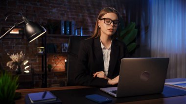Odaklanmış bir iş kadını masasında strateji düşünüyor. Ofis modern, dizüstü bilgisayarı ve düzgün düzenlenmiş belgeleri var..