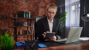 Odaklanmış bir iş kadını masasında strateji düşünüyor. Ofis modern, tablet ve belgeler düzgünce düzenlenmiş..