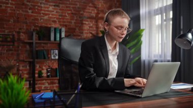 Odaklanmış bir iş kadını masasında strateji düşünüyor. Ofis modern, dizüstü bilgisayarı ve düzgün düzenlenmiş belgeleri var..