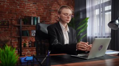 Takım elbiseli iş kadını rahat bir şekilde şık bir ofiste tuğladan duvarlarla oturuyor..