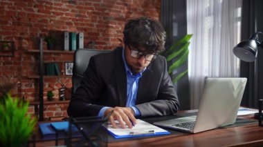 Kendini işine adamış bir birey, modern ofis ortamında bir masaya notlar yazarken görülüyor. Konsantrasyon ve verimliliği vurguluyor..