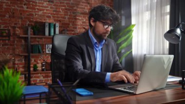 Takım elbiseli bir işadamı, modern ofis ortamında tuğla duvarlar ve dekorlarla dizüstü bilgisayarına odaklanmıştı..