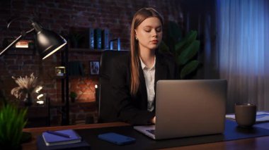 Odaklanmış bir iş kadını masasında strateji düşünüyor. Ofis modern, dizüstü bilgisayarı ve düzgün düzenlenmiş belgeleri var..