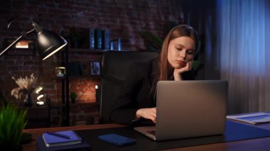 Masasında odaklanmış iş kadını düşünme stratejisi, yorgun görünüyor. Dizüstü bilgisayarı ve düzgün düzenlenmiş belgeleri olan modern ofis.