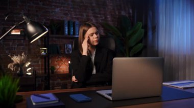 Ofiste bir kadın gece geç saatlerde masasında oturur, dizüstü bilgisayara bakarken düşünür. Yoğun bir şekilde odaklanmış görünüyor. Önemli bir iş ya da karar verme sürecinde olduğunu gösteriyor..
