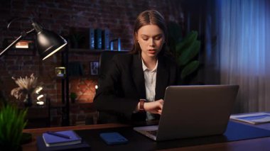 Odaklanmış bir iş kadını masasında strateji düşünüyor. Ofis modern, dizüstü bilgisayarı ve düzgün düzenlenmiş belgeleri var..