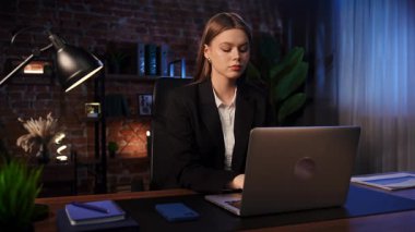 Masasında şık, modern bir ofis ortamında akıllı telefon kullanan takım elbiseli genç bir kadın..