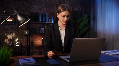 Odaklanmış bir iş kadını masasında strateji düşünüyor. Ofis modern, dizüstü bilgisayarı ve düzgün düzenlenmiş belgeleri var..