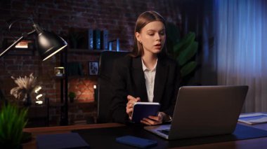 Kendini işine adamış bir birey, modern ofis ortamında bir masaya notlar yazarken görülüyor. Konsantrasyon ve verimliliği vurguluyor..