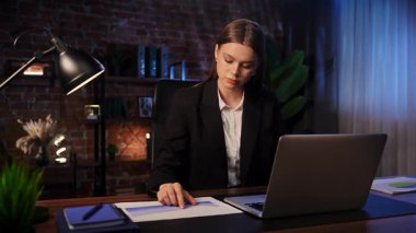 Geç saatlere kadar şık tuğlalı bir ofiste çalışan genç bir iş kadını, önünde bir dizüstü bilgisayarla görevlerine odaklanmış..