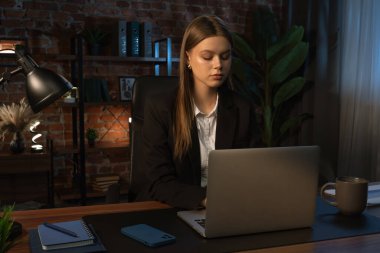 Odaklanmış bir iş kadını masasında strateji düşünüyor. Ofis modern, dizüstü bilgisayarı ve düzgün düzenlenmiş belgeleri var..