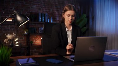 Takım elbiseli iş kadını rahat bir şekilde şık bir ofiste tuğladan duvarlarla oturuyor..