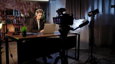 Sahne arkasında. Kulaklık takan genç bir kadın, kitaplarla ve bitkilerle çevrili modern ofis ortamında dizüstü bilgisayarına odaklanıyor..