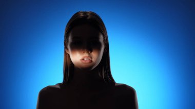 Yüzünde gölgeler olan bir kadının dingin portresi, canlı mavi bir arkaplan üzerine kurulmuş..