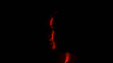 Bir insan yüzü silueti, çarpıcı bir kırmızı ışık huzmesi tarafından karanlık bir arka plana doğru aydınlatılır ve gizem uyandırır..