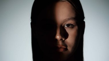 Bir kadının yüzünü gösteren çarpıcı bir portre. Işık huzmesi ve gölgeyle bölünmüş, dramatik ve gizemli bir etki yaratıyor..