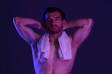 Üstsüz bir adam, omuzlarında havluyla, kendine güvenen bir şekilde poz veriyor.