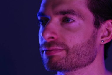 Sakallı bir adamın portresi. Mor ve mavi neon ışıklarla aydınlatılmış. Yüzüne ve boynuna odaklanmış..