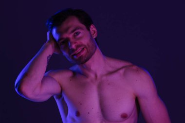 Üstsüz bir adam, mor ışığın altında poz veriyor.