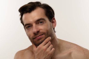 Düşünceli bir ifade sergileyen bir adamın portresi. Kısa saçları ve bir küpesi var. Benzersiz tarzının altını çiziyor..