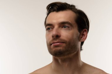 Düşünceli bir ifade sergileyen bir adamın portresi. Kısa saçları ve bir küpesi var. Benzersiz tarzının altını çiziyor..