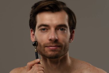 Bir adam alnında siyah yeşim bir silindir kullanıyor. Cilt bakımının bir parçası olarak yüz gençleştirme için..